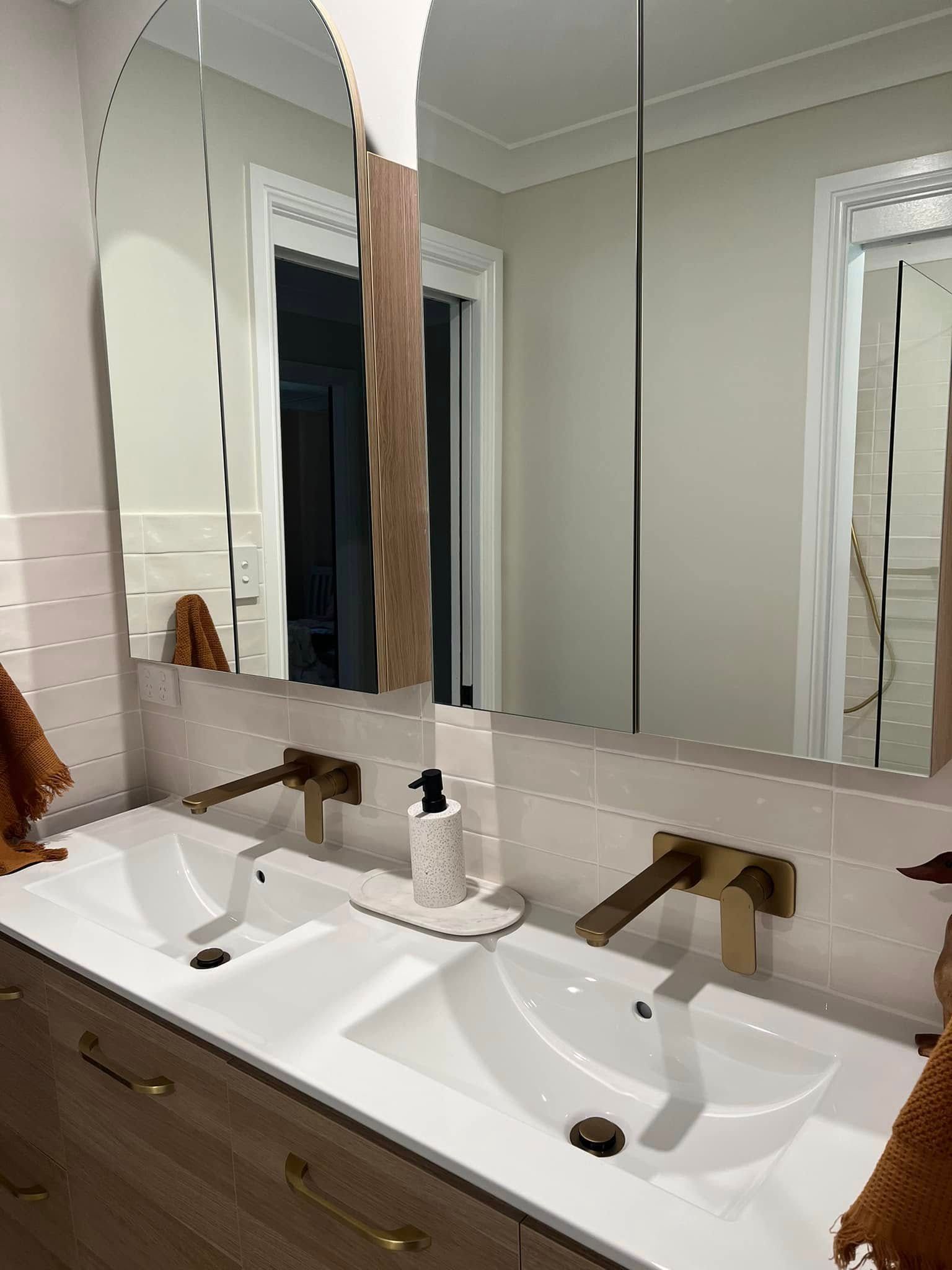 Bathroom vanity with double sinks, large mirror, and bronze faucets against light gray walls