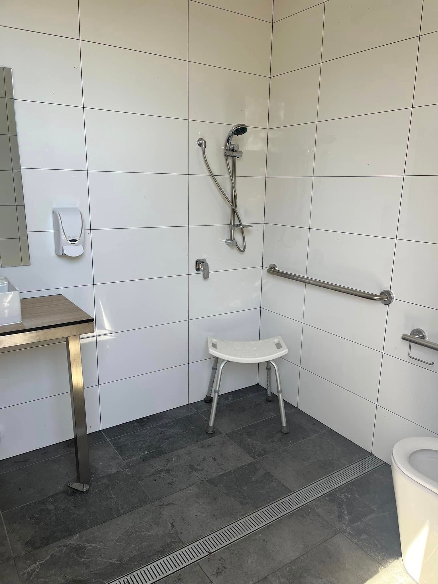Accessible bathroom with tiled walls, shower seat, grab bar, and floor drain