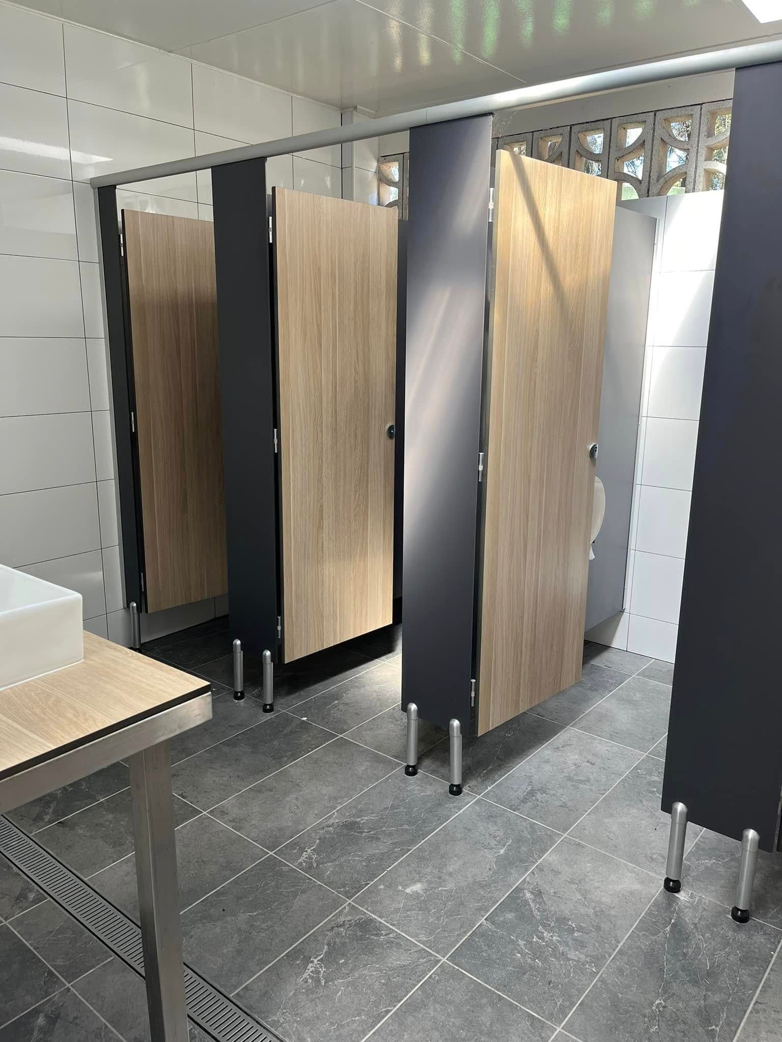 Row of light wood restroom stall doors with black partitions in a tiled bathroom