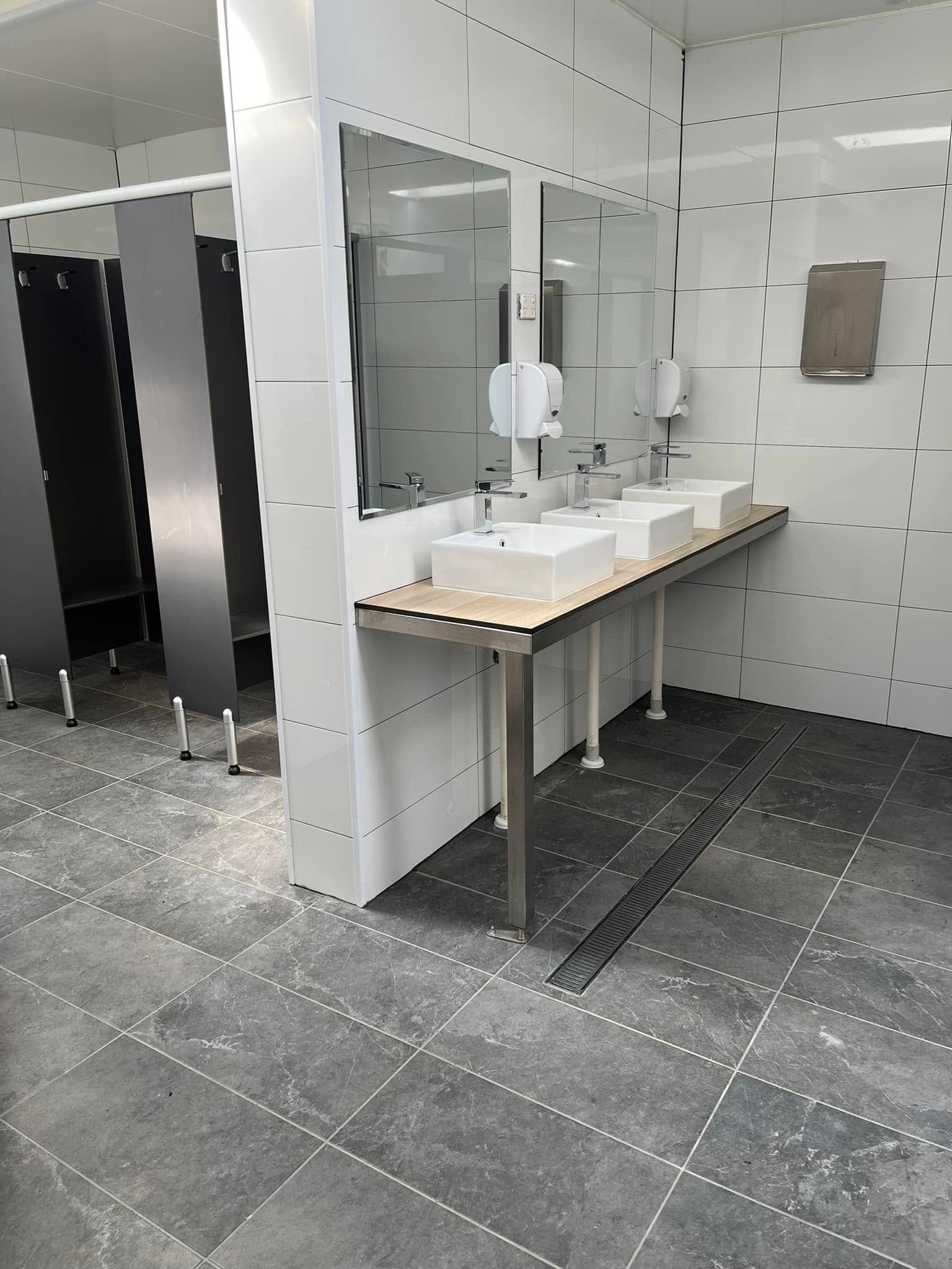 Public restroom with sinks, mirrors, and stalls; one stall door is open on the left.