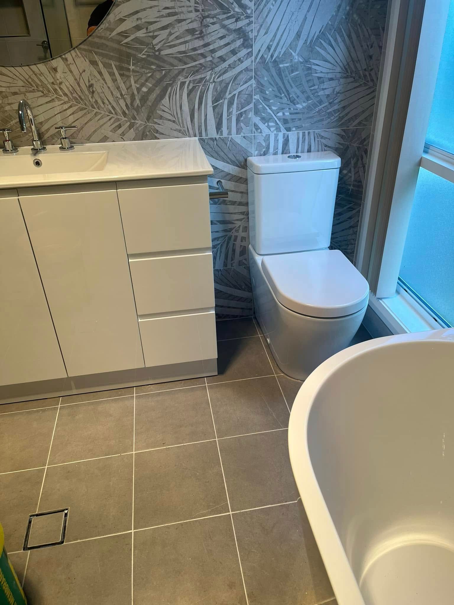 Modern bathroom with white vanity, toilet, freestanding tub, and gray patterned tile floor and wall.