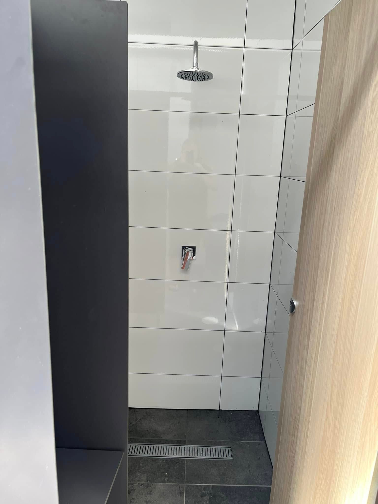 Narrow tiled shower stall with a showerhead, drain, and dark and beige walls