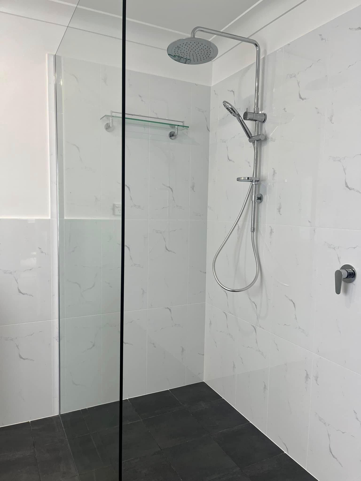 Modern walk-in shower with glass panel, white tiled walls, black floor, and handheld showerhead