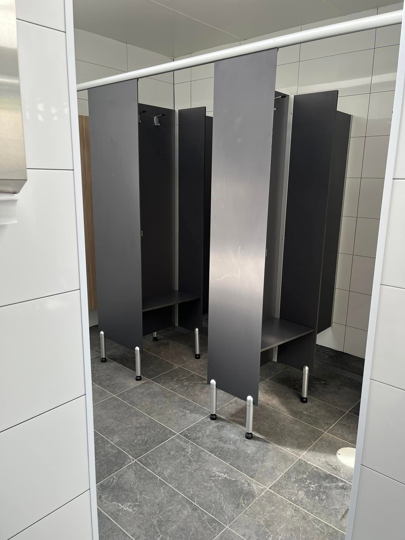 Public restroom stalls with dark doors and white tiled walls in a clean, bright interior.