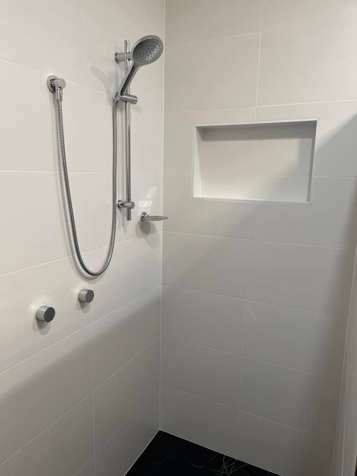 Accessible shower corner with handheld showerhead, grab bars, and built-in wall niche