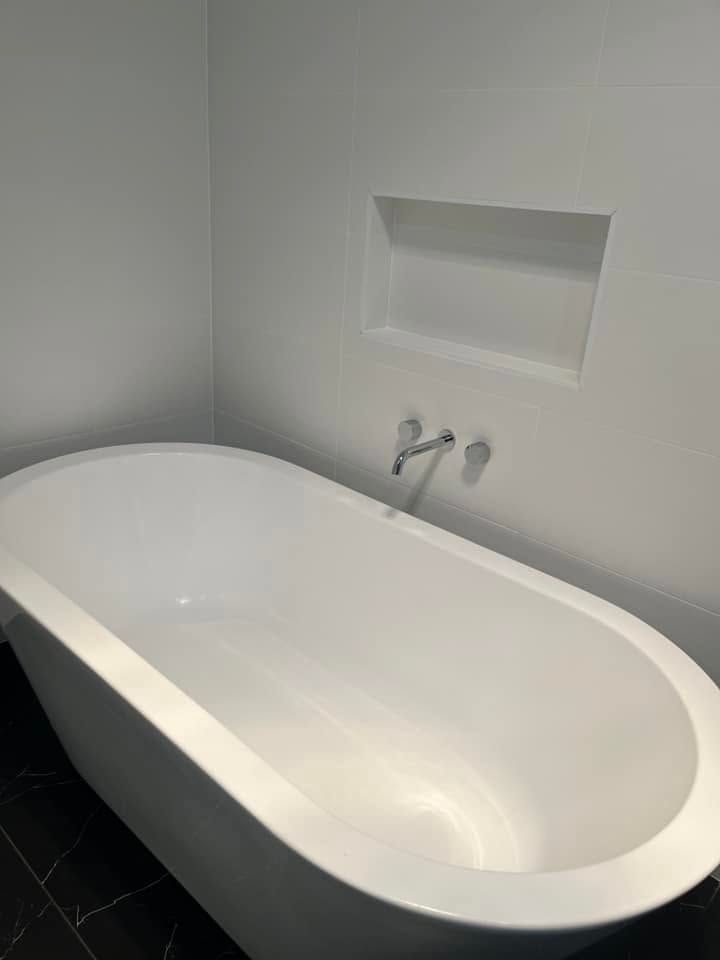 Freestanding white bathtub in a minimalist bathroom with a wall niche and chrome faucet.