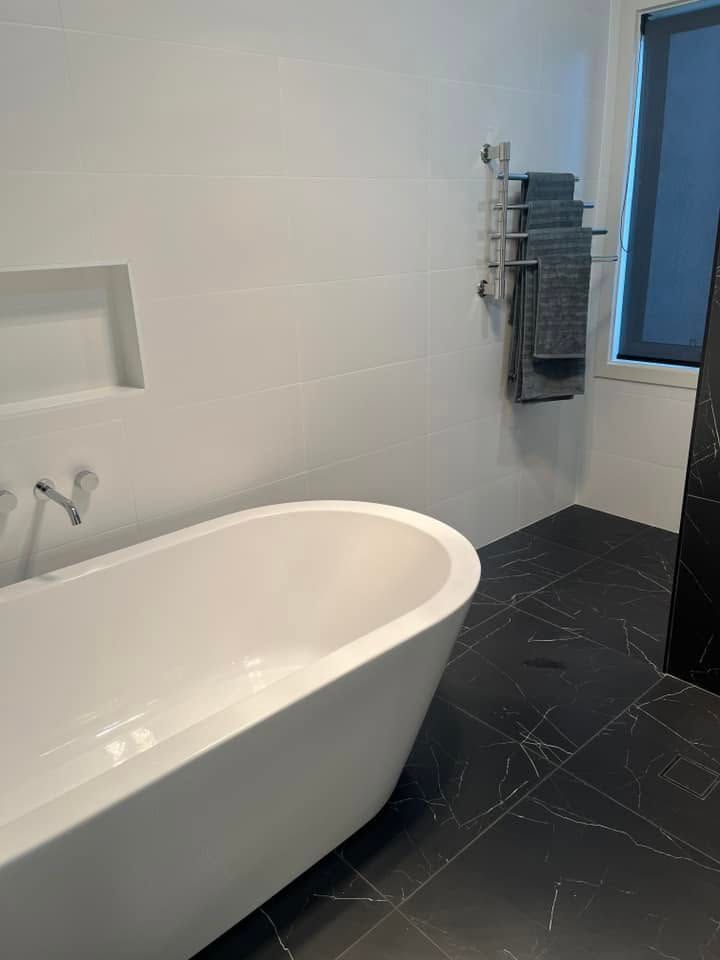 Modern bathroom with a white freestanding bathtub, black tiled floor, and towel rack by a window