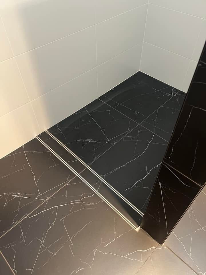 Corner of a tiled shower with dark floor tiles, light wall tiles, and a raised step.