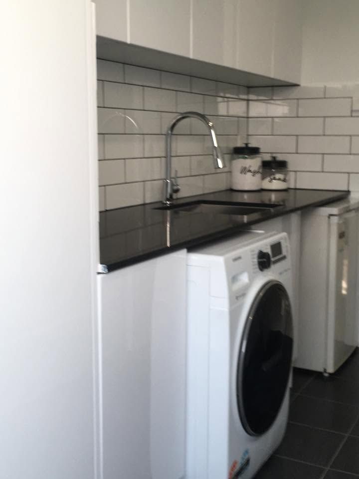 Compact white kitchen with black countertop, subway tile backsplash, sink, and washing machine under the counter