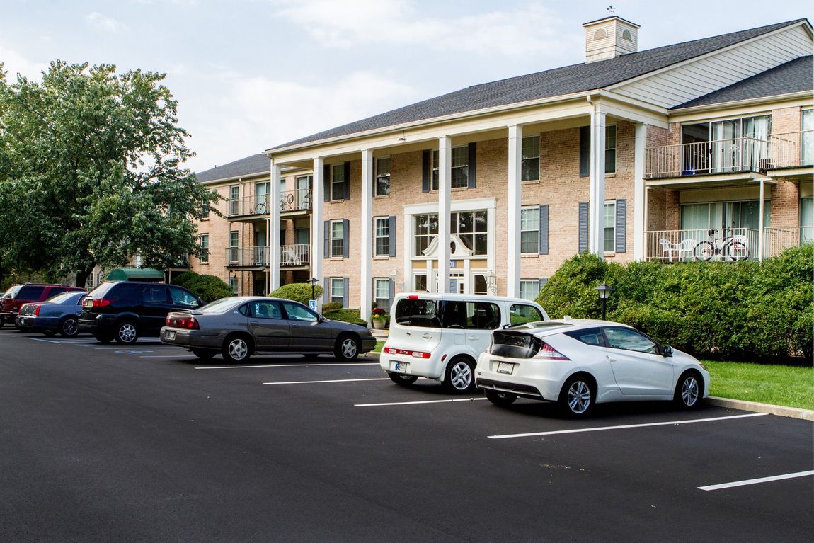 Cars parked in front of a brick apartment building with white columns and balconies.