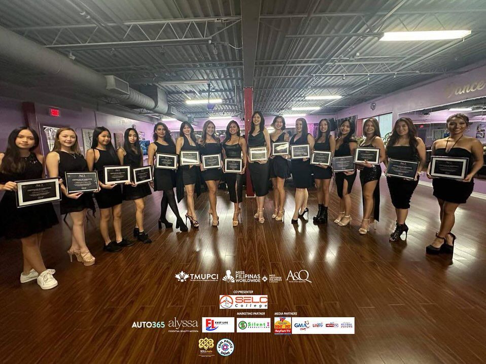 Group of women in black dresses, holding framed awards, in a dance studio.