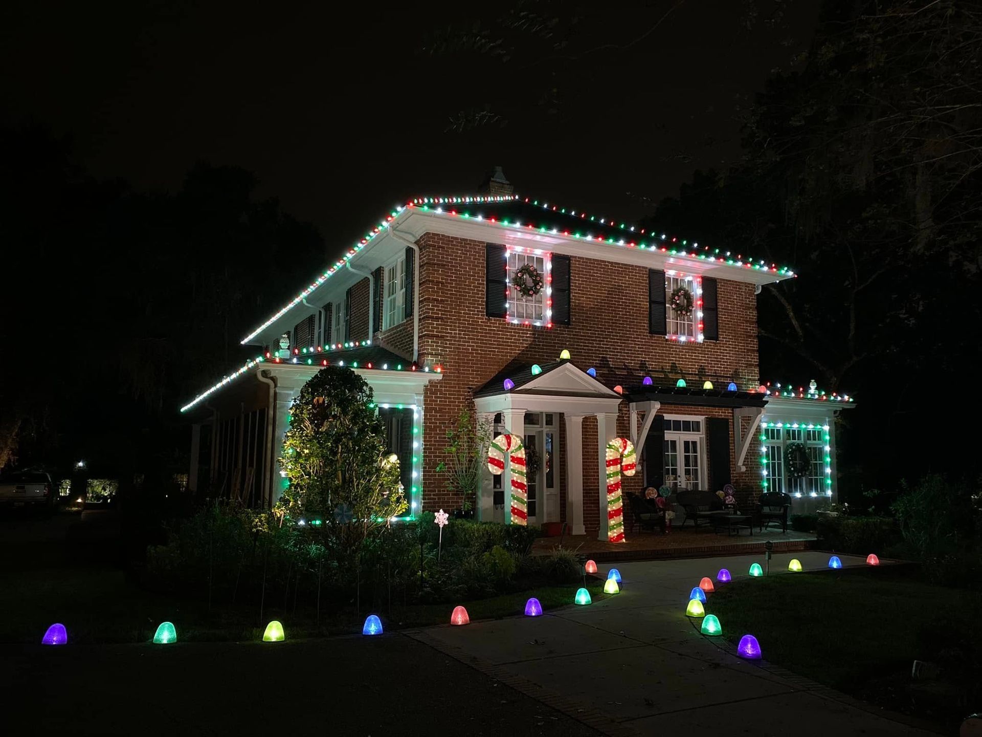 Two-story house at night decorated with colorful Christmas lights and glowing lawn ornaments