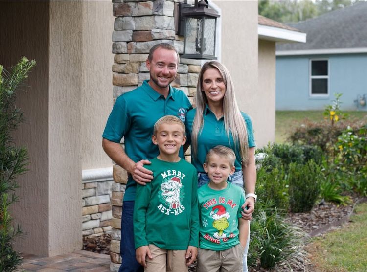 Family of four posing outside a house, smiling and standing by a stone pillar.