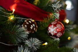 Christmas tree with red ribbon, pinecones, and a red ornament with white snowflakes and lights