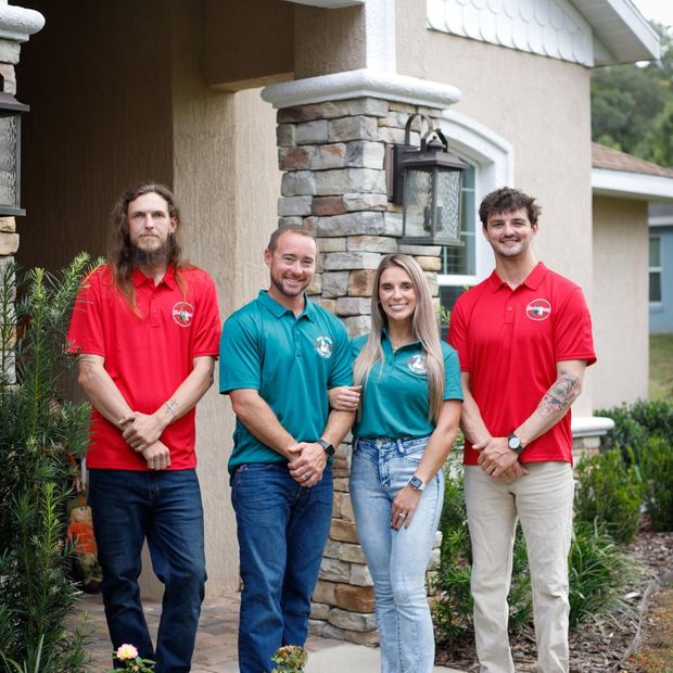 Four people standing outside a building, two in red shirts, one in teal, and one in a gray top.