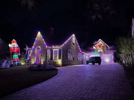 House and driveway covered in colorful Christmas lights, with a large Santa decoration at the left.