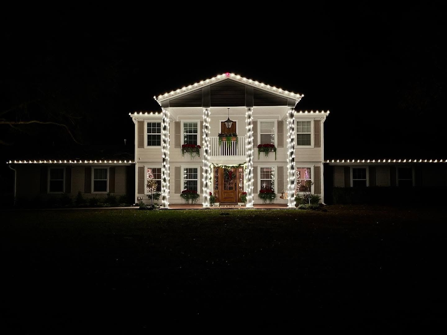 Illuminated white mansion at night with a lit roofline against a dark sky