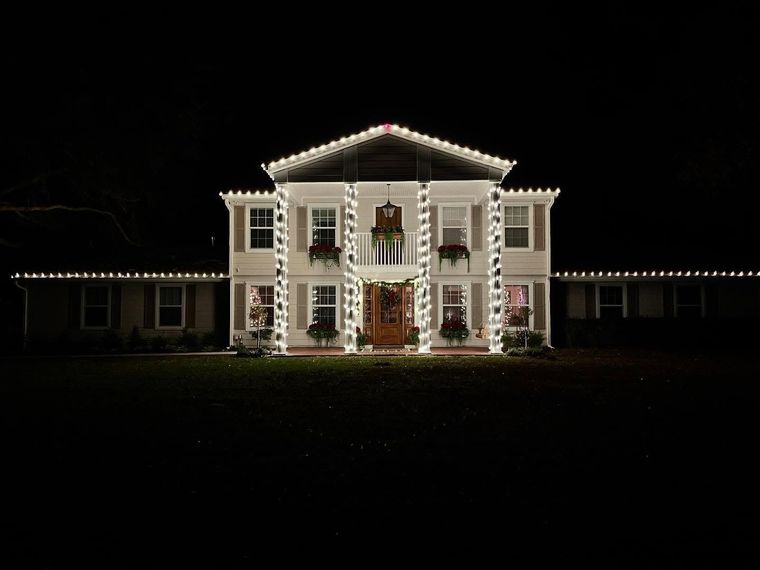 Illuminated white mansion at night with a lit roofline against a dark sky