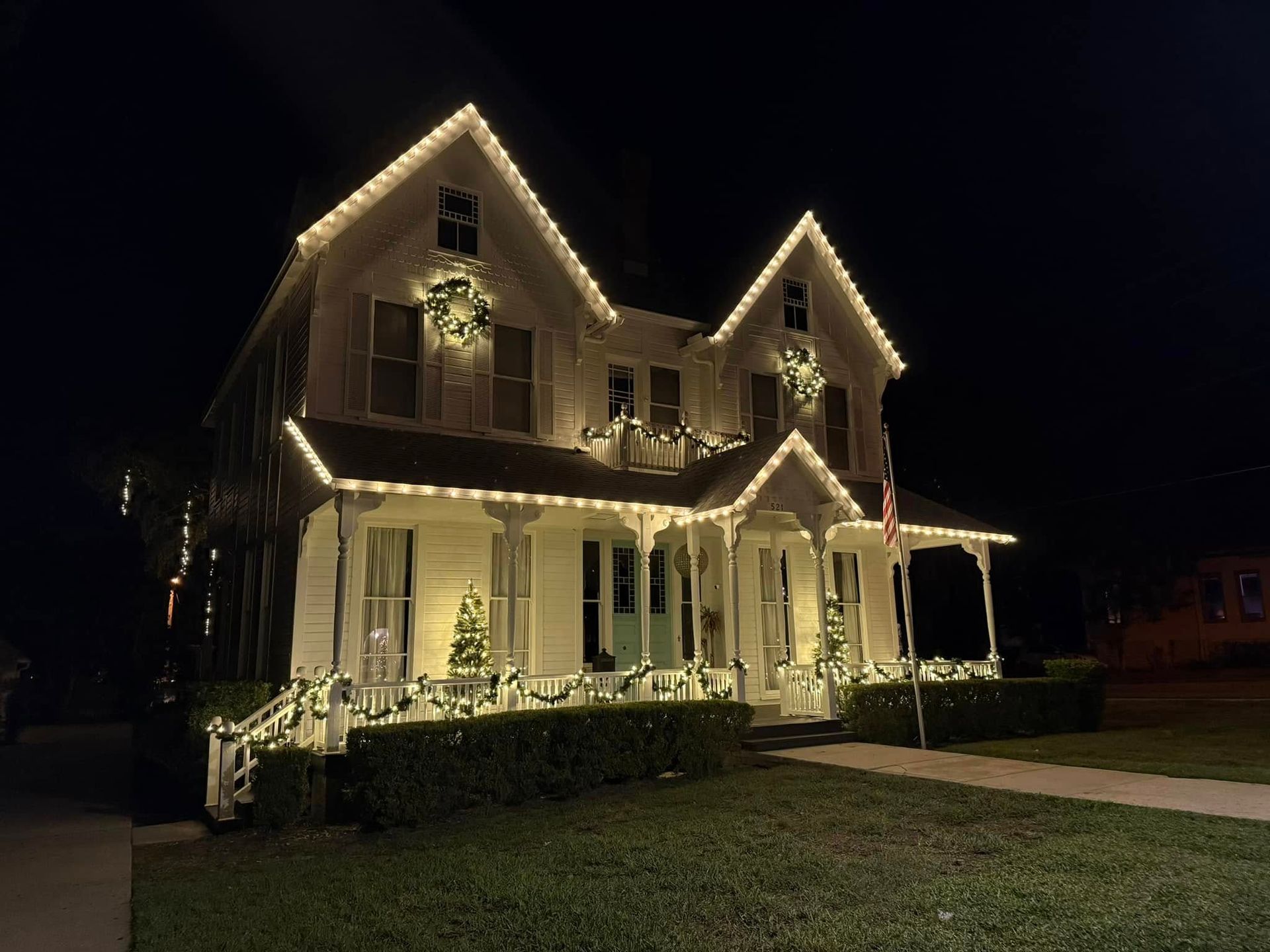 Two-story house at night outlined with warm white holiday lights on the roof and porch
