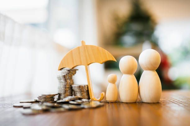 A wooden family standing next to a pile of coins under an umbrella.