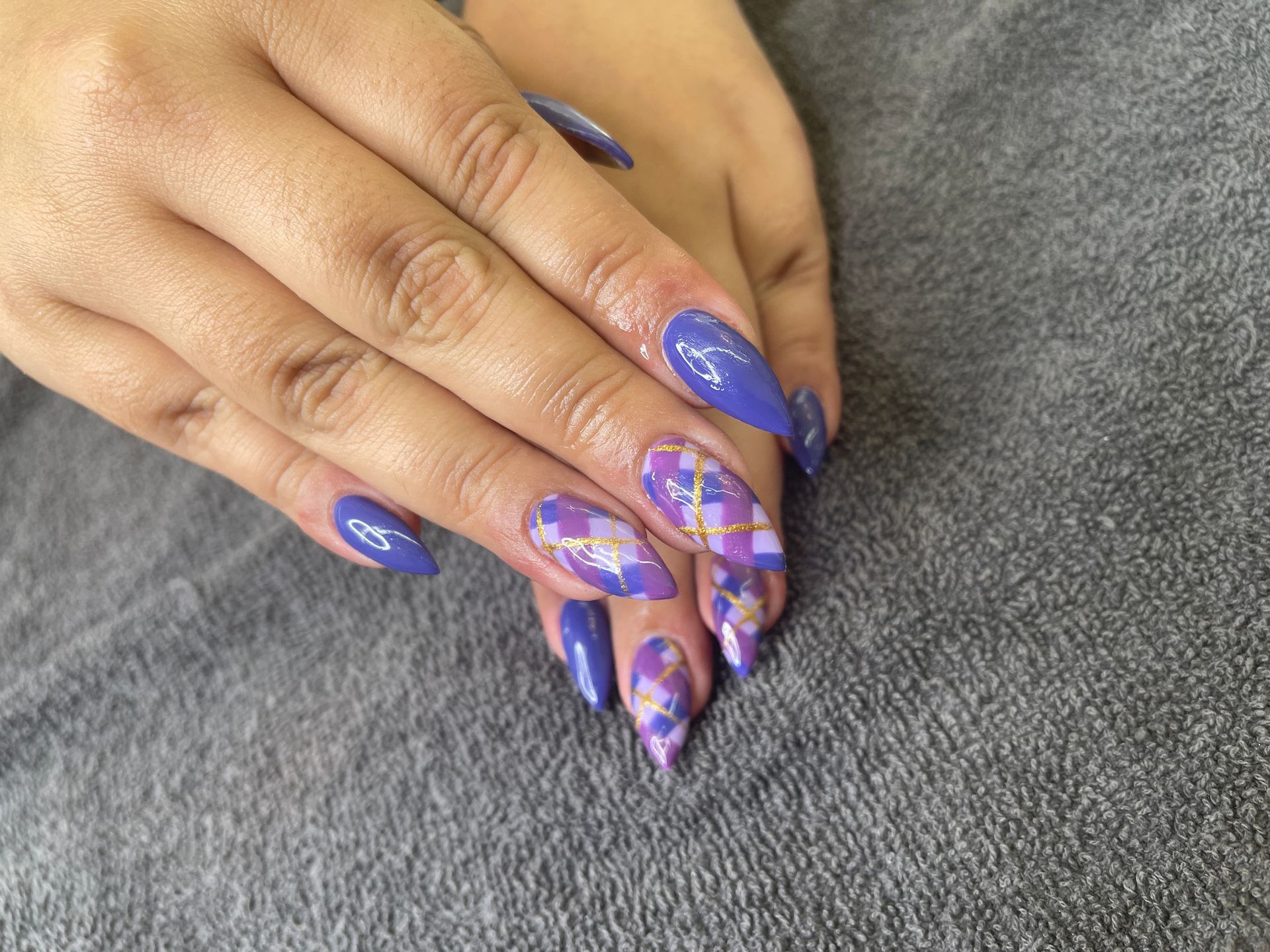 Hands with blue and purple patterned acrylic nails resting on a gray surface.