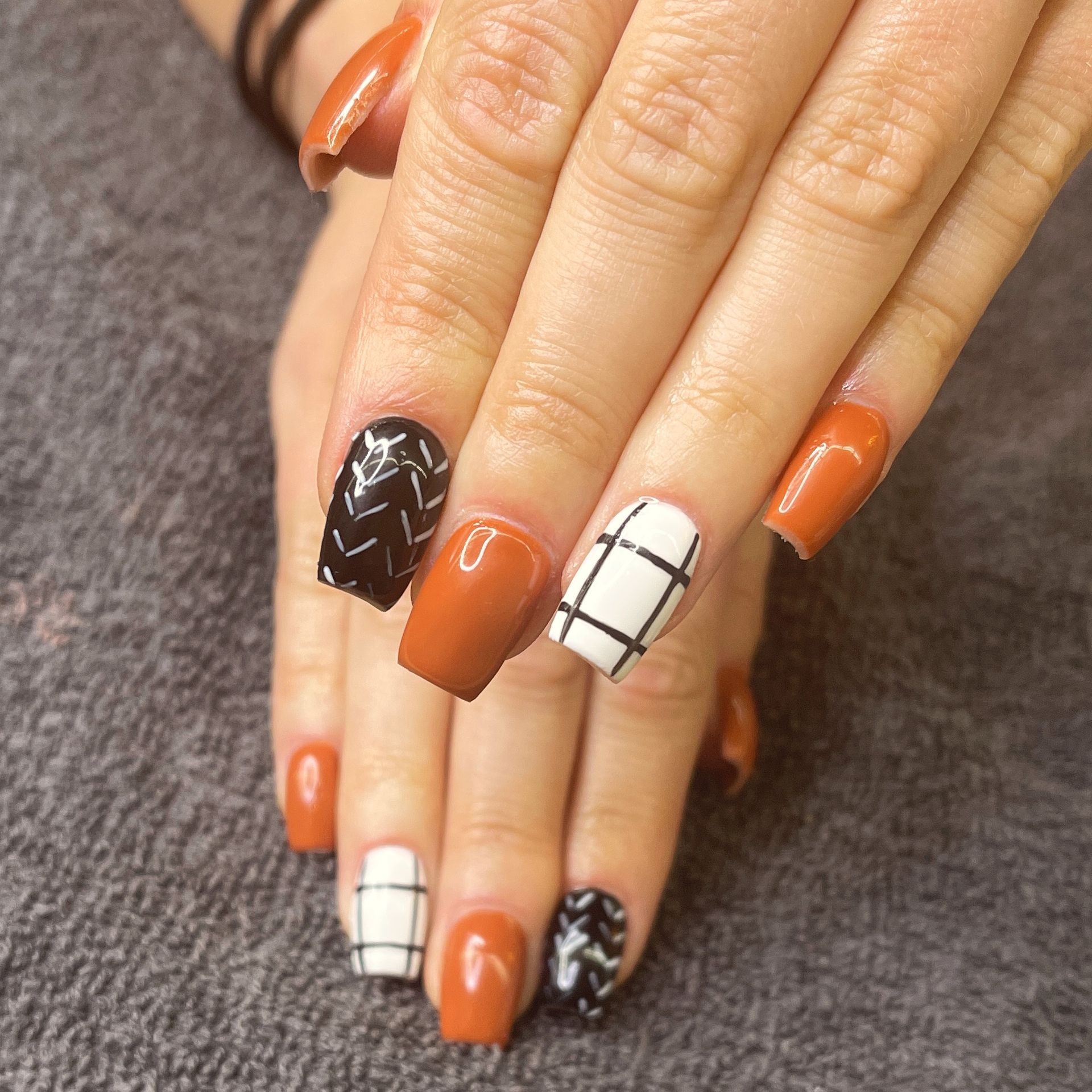 Hands with orange, black, and white patterned manicured nails resting on a gray fabric surface