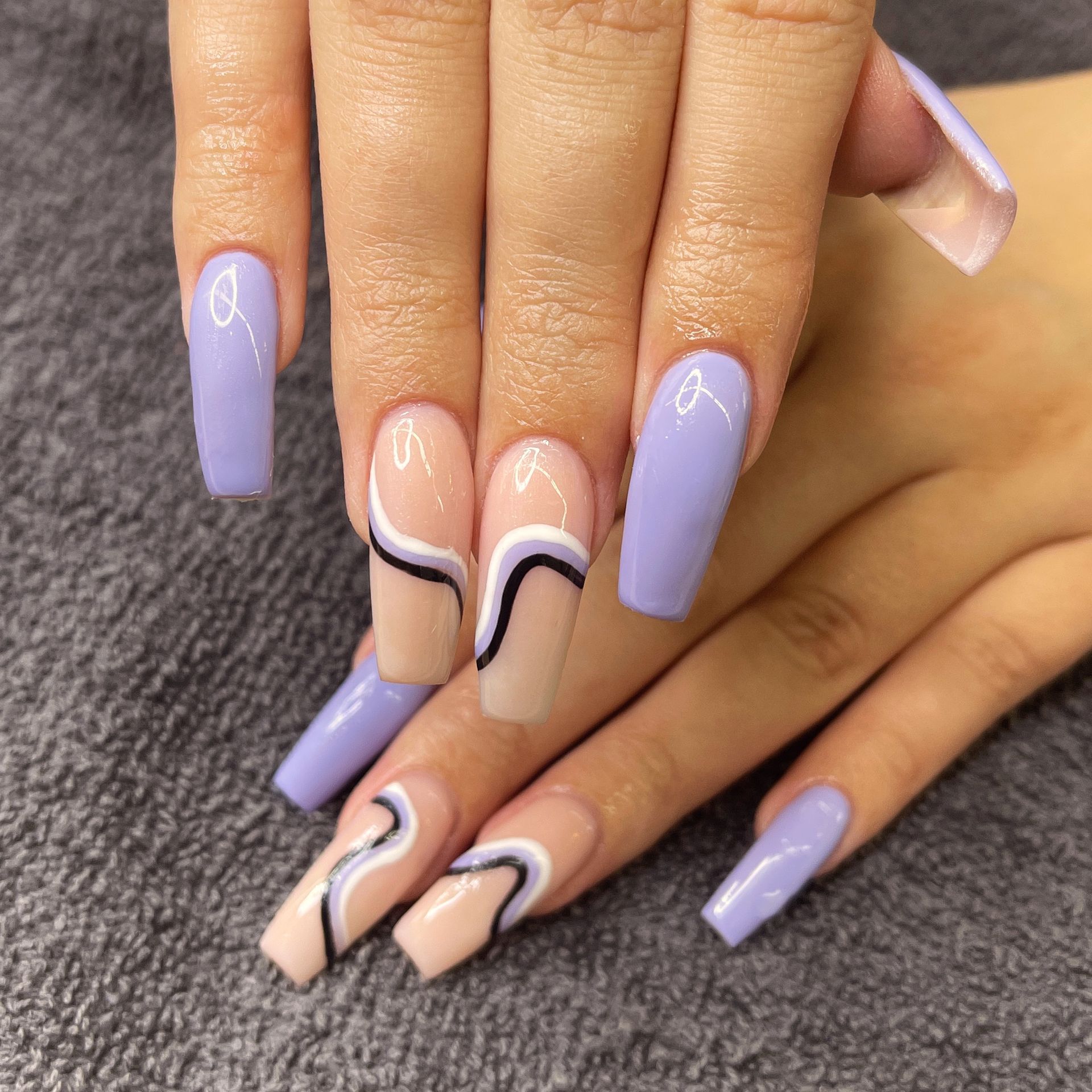 Hands with long lavender and nude nails featuring black wave accents.