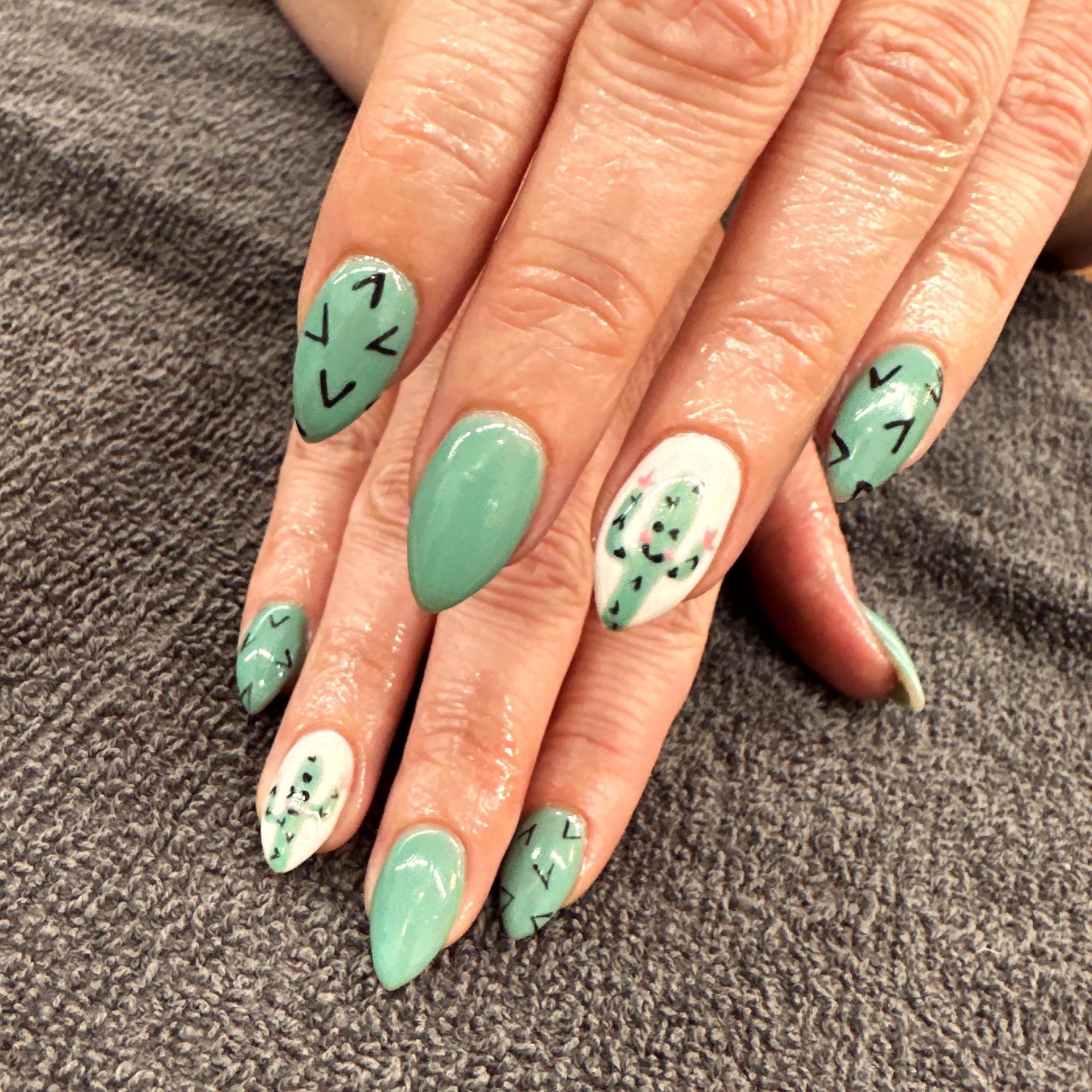 Hand with mint green nails and black geometric accents on a gray fabric background