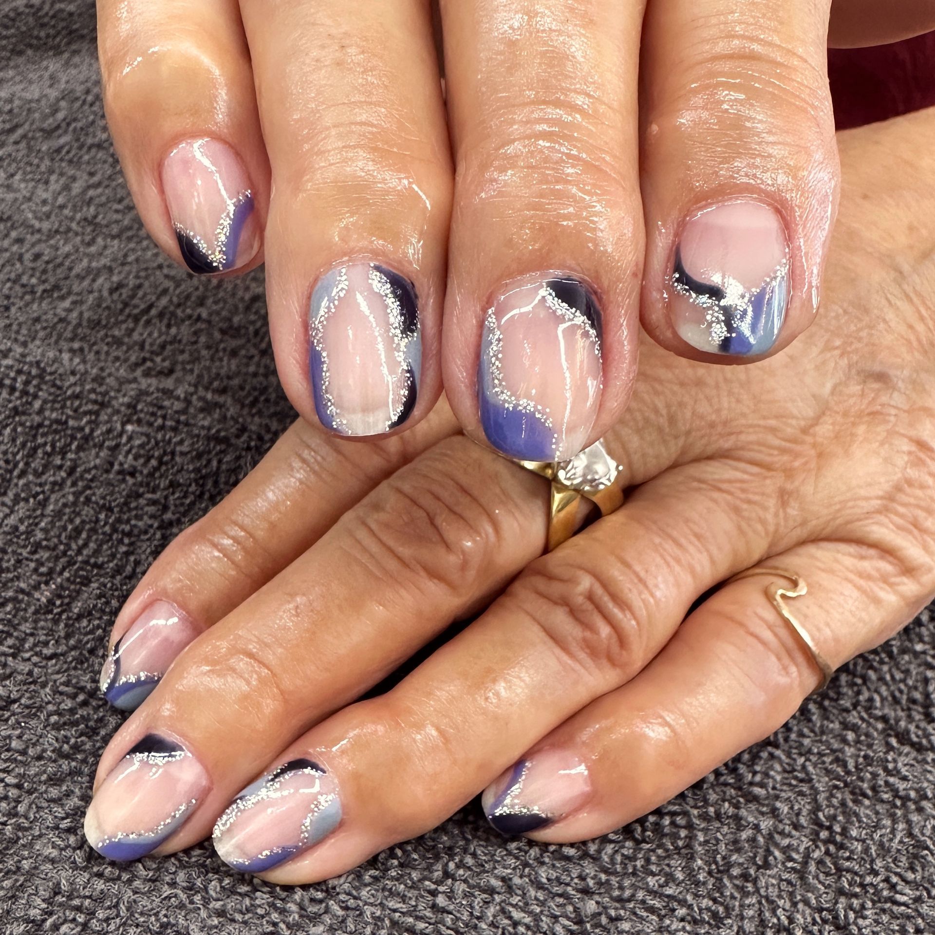 Close-up of hands with glossy nude, blue, and black marbled manicured nails.