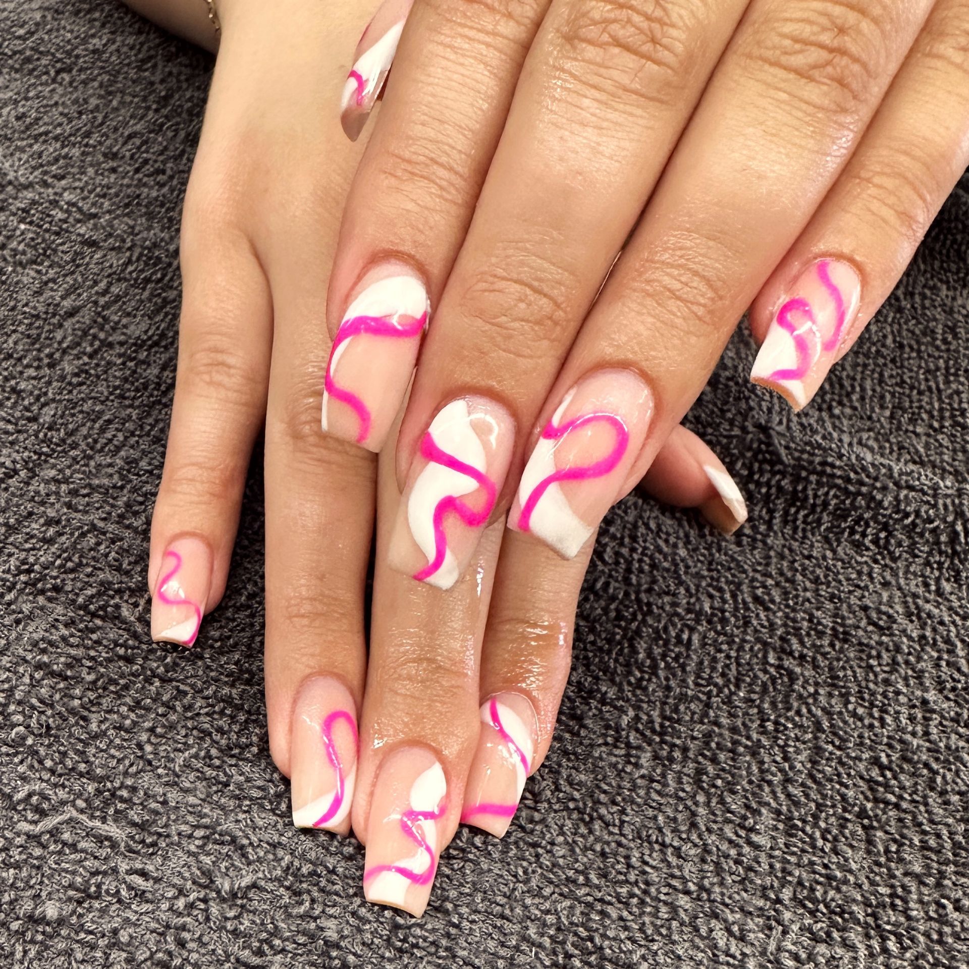 Hands with long nude nails featuring pink swirl nail art resting on a dark textured surface