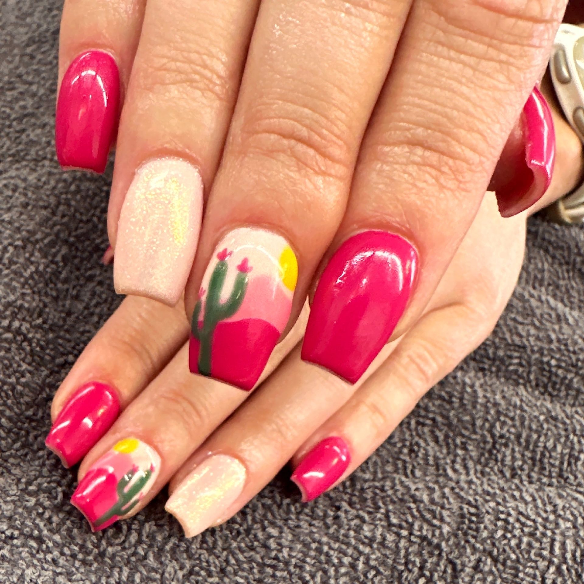 Hands with bright pink and floral nail art resting on a gray towel
