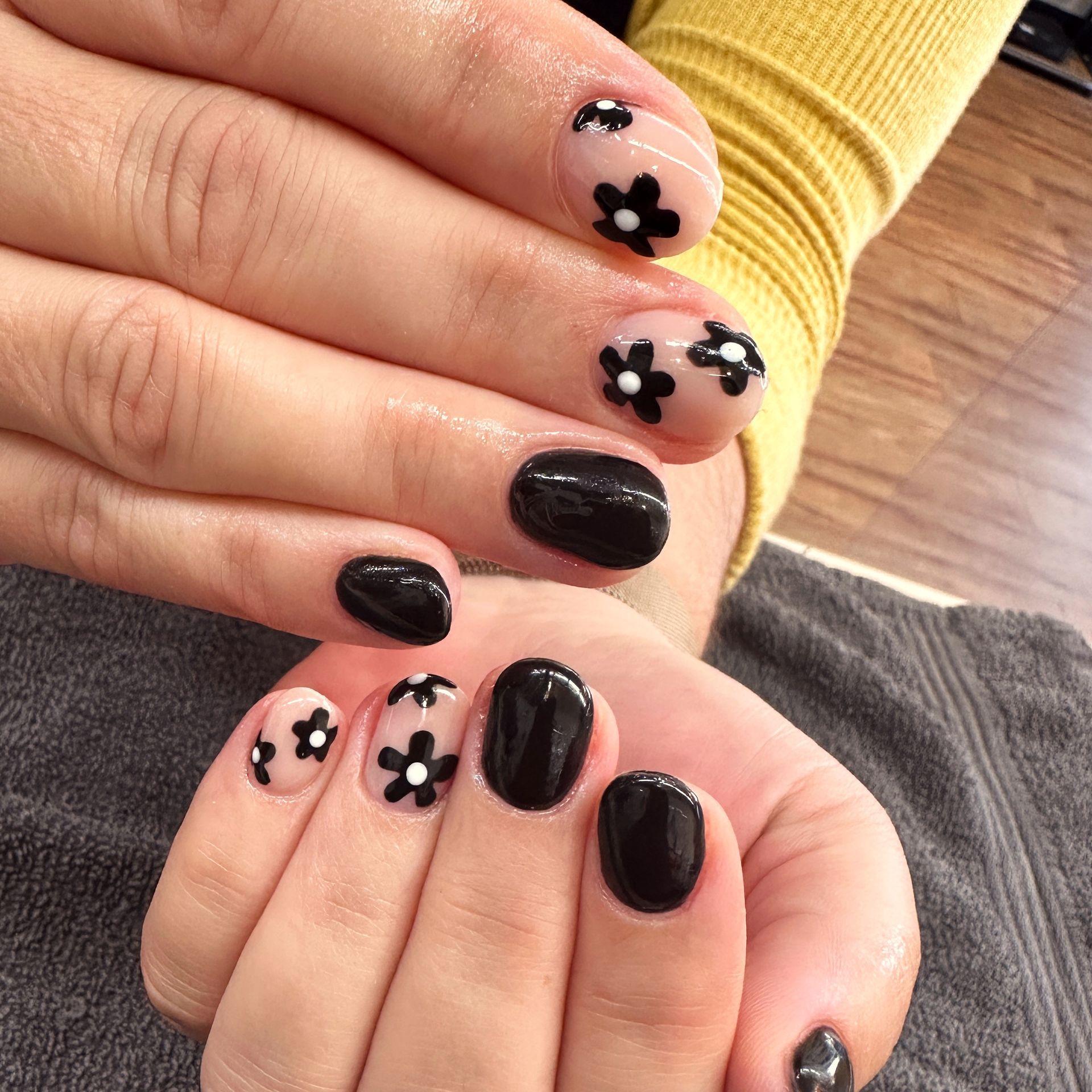 Hands with black and pink daisy nail art, shown together over a gray and yellow background.