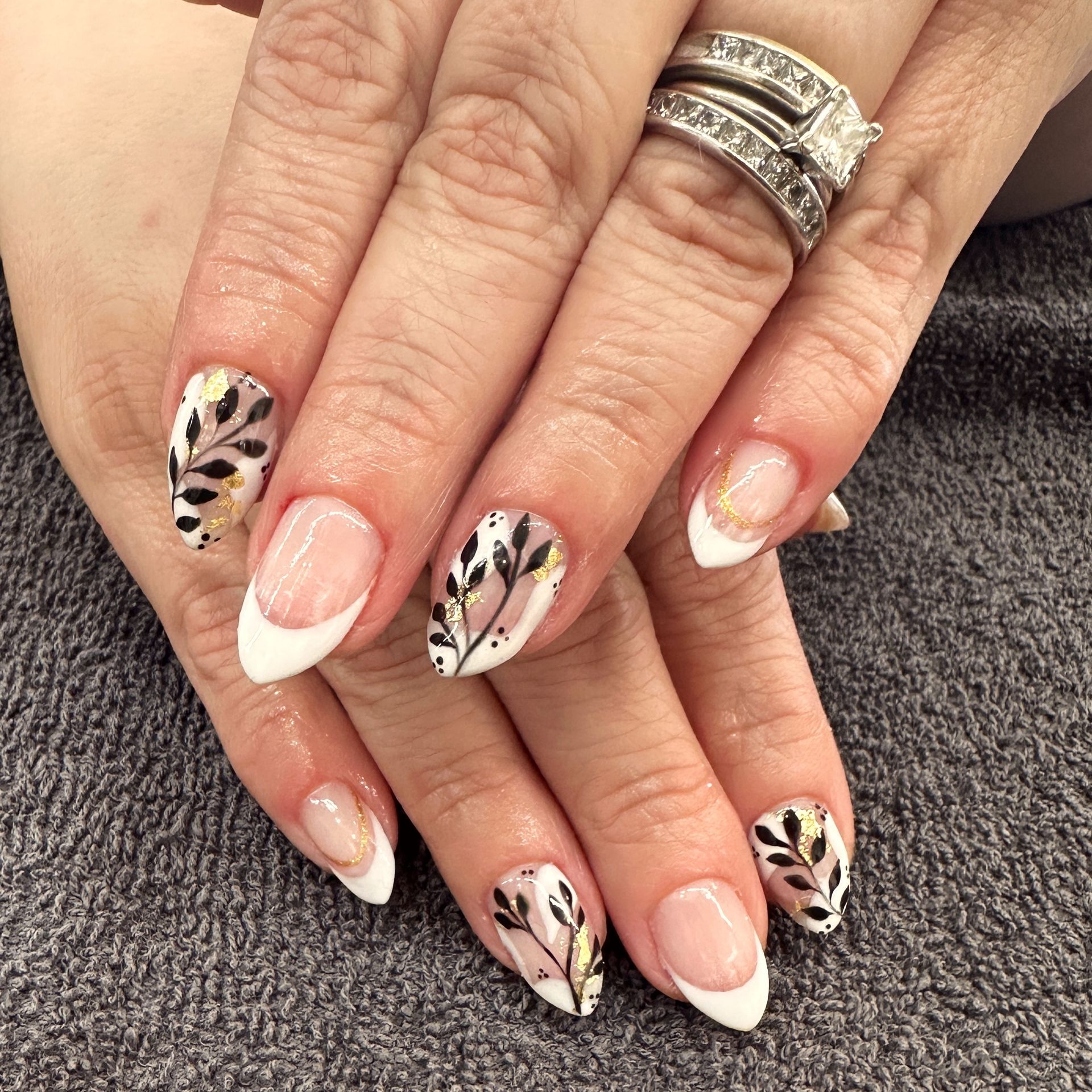 Hand with white and leopard-print French tip manicure and silver ring on gray towel