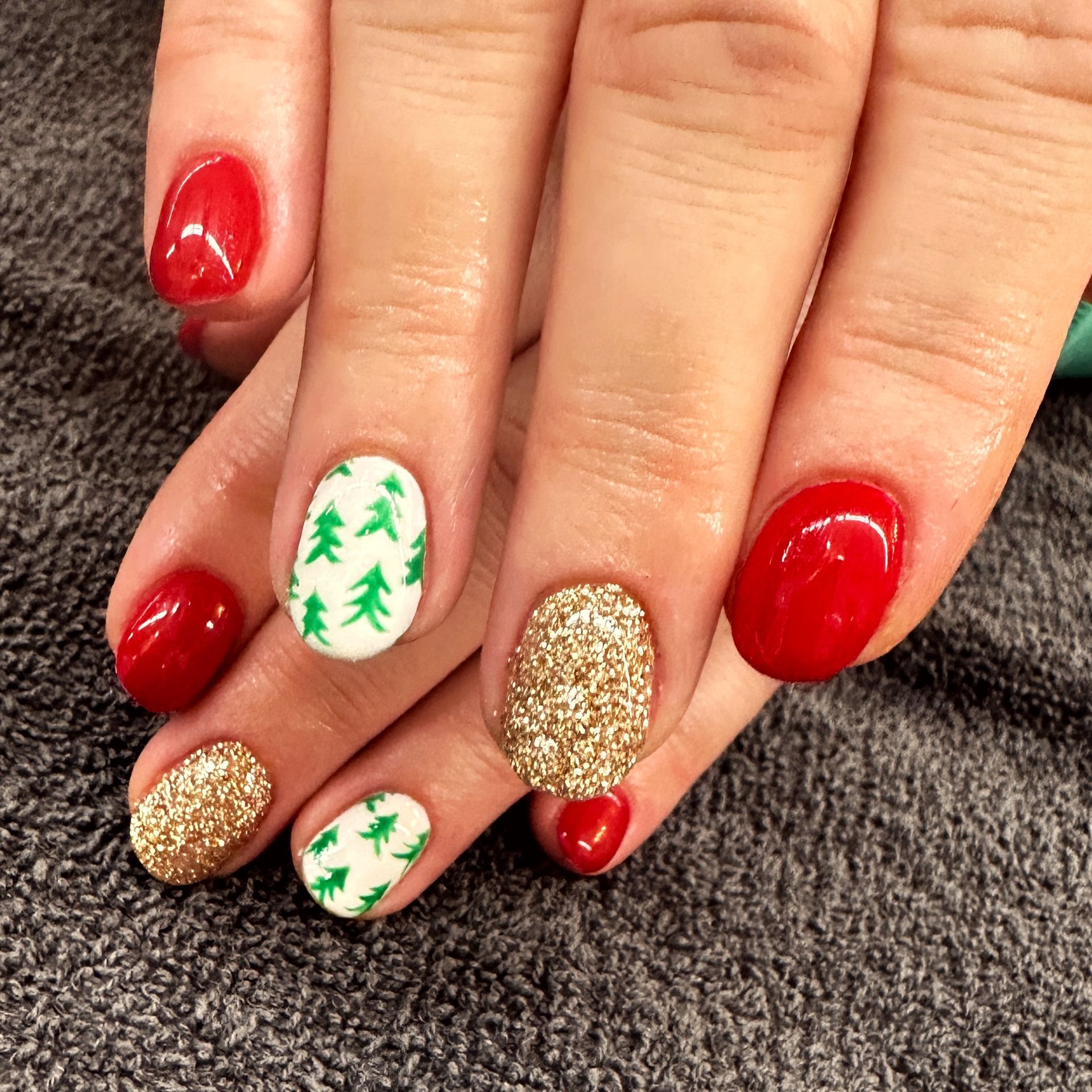 Hands with festive red, gold glitter, and white nails with green Christmas tree designs.