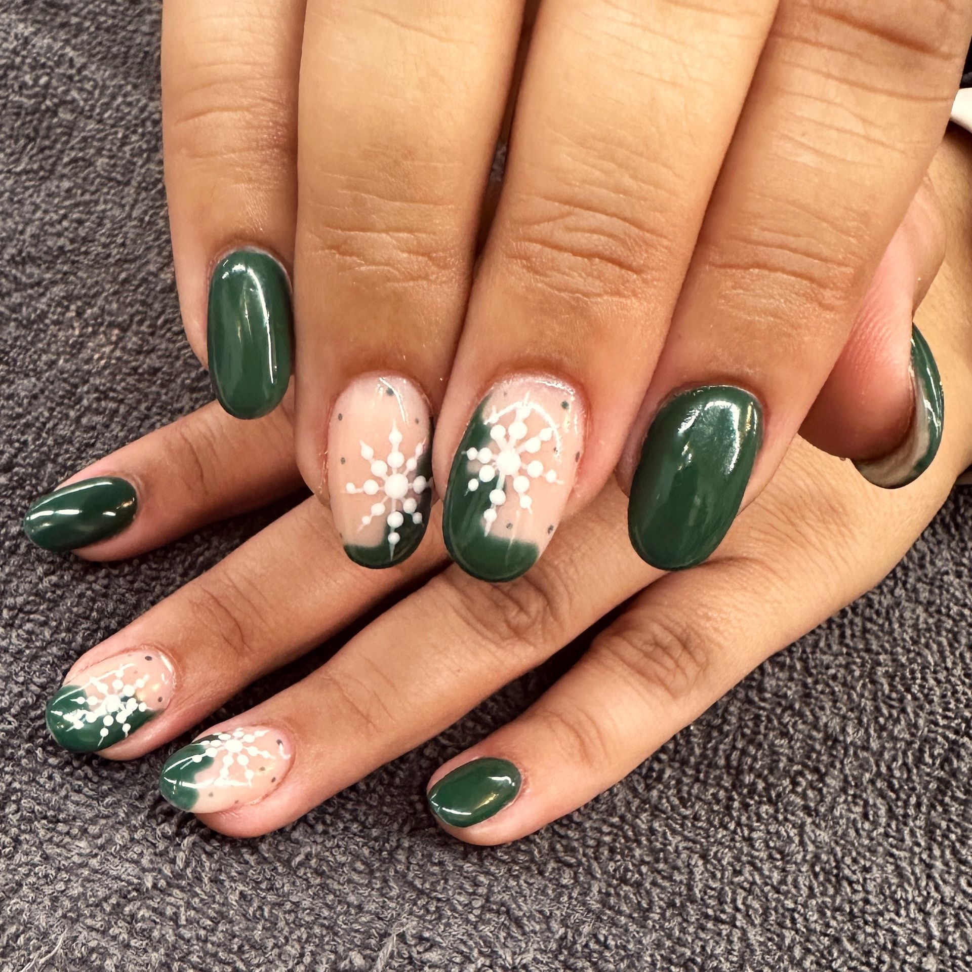 Hands with dark green nails and floral accent nail art on a textured gray surface