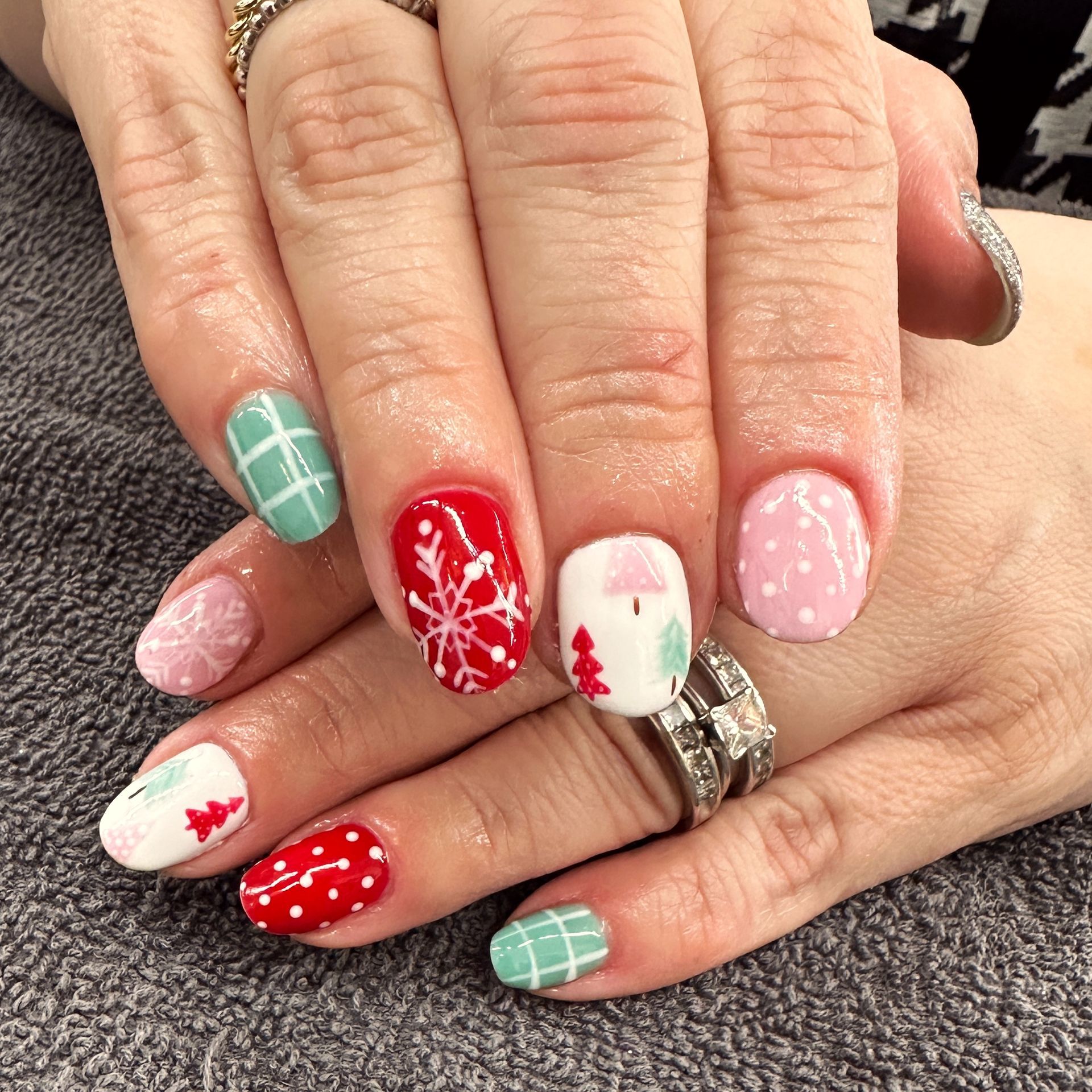 Hand with festive holiday manicure in red, green, white, and pink nail art.