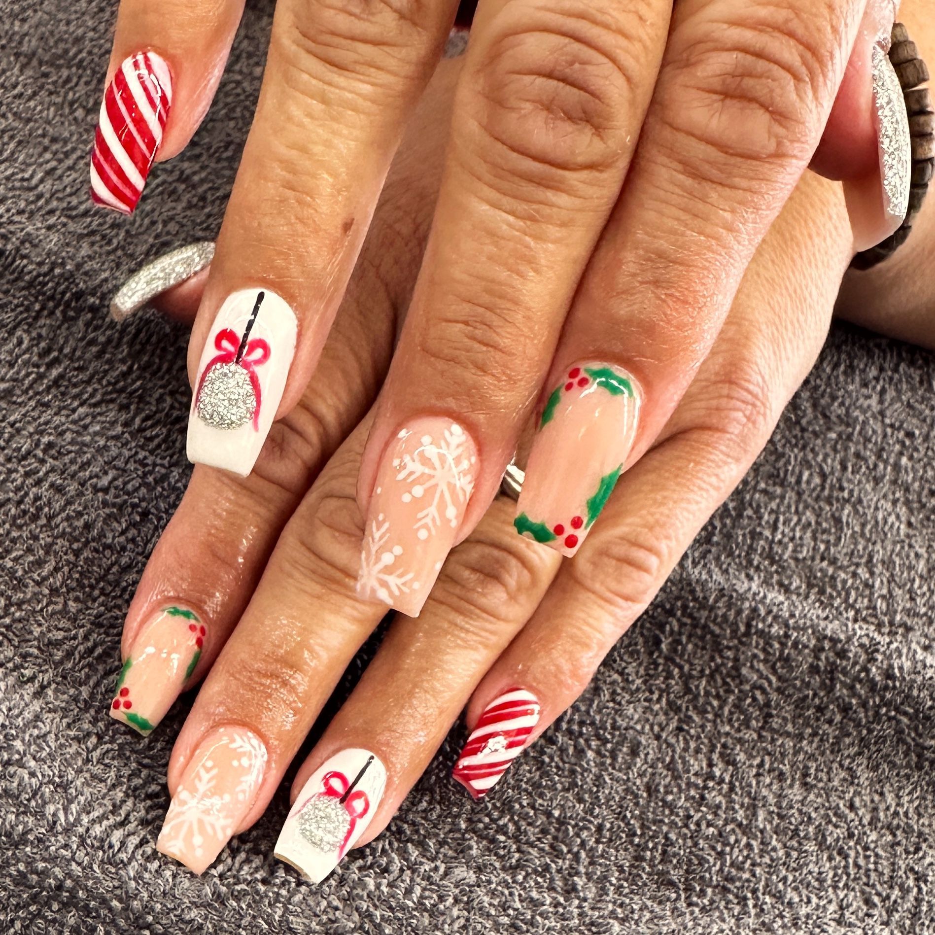 Hand with festive holiday nail art in red, white, and nude tones with candy cane and bow designs