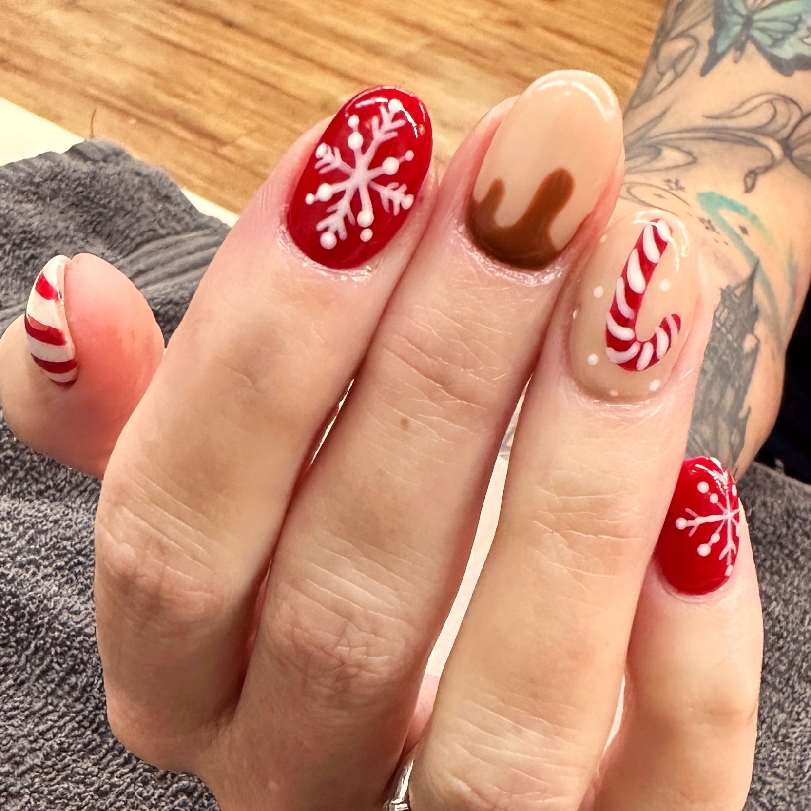 Hand with red, white, and brown holiday-themed nail art, including snowflakes and candy cane designs.