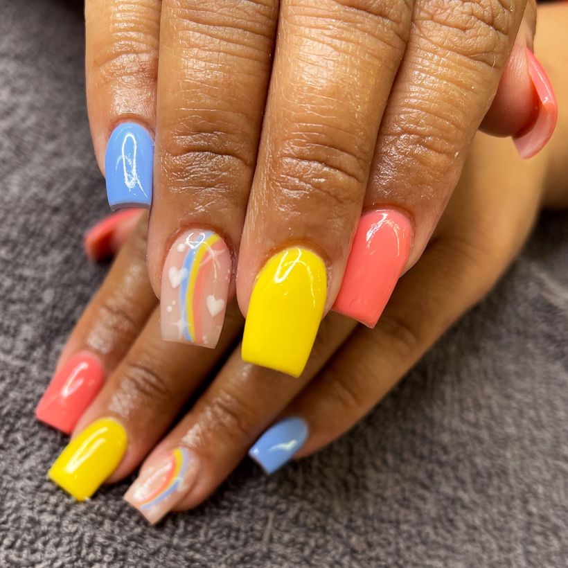 Hands with colorful manicured nails in blue, yellow, coral, and pastel stripes on a gray surface