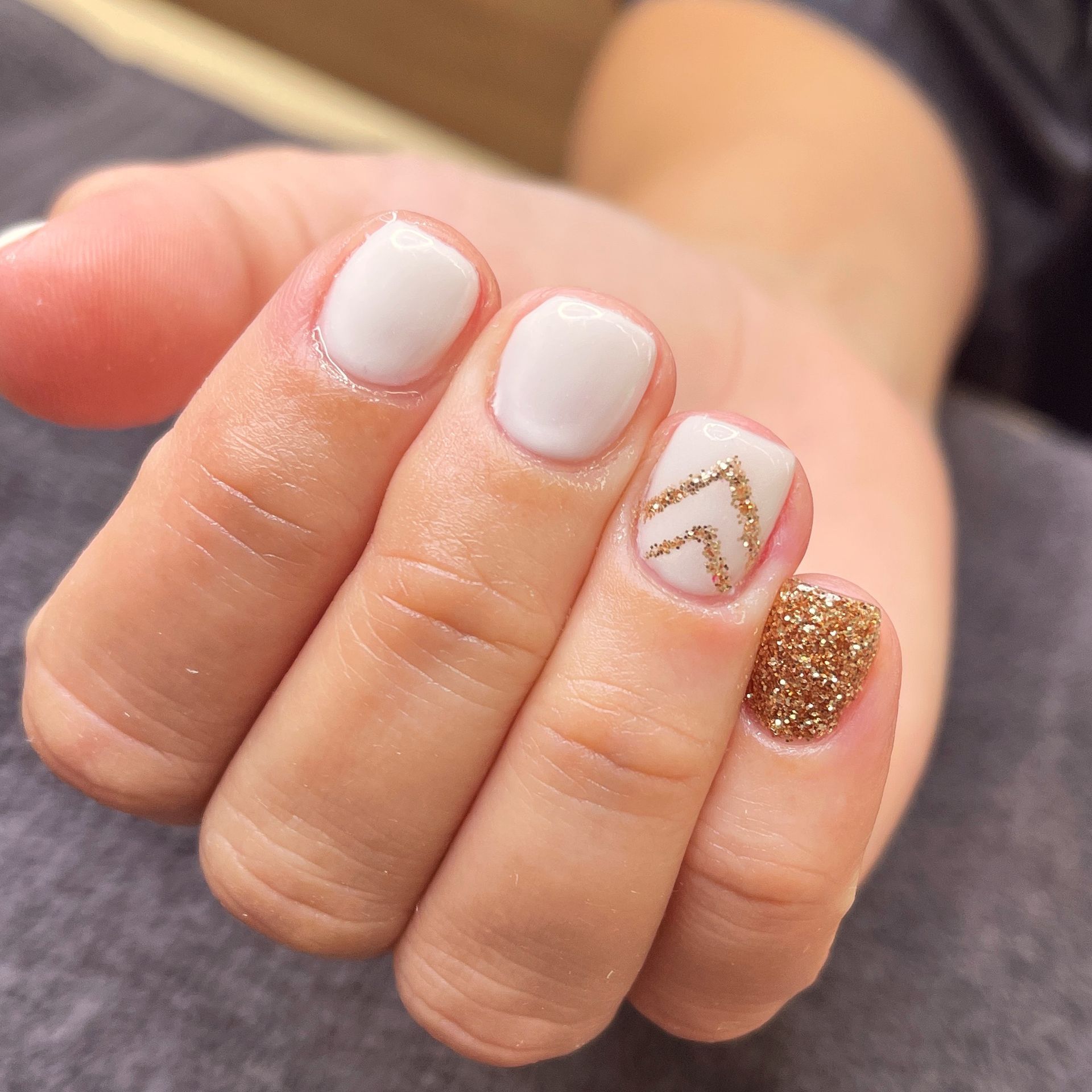 Close-up of manicured hand with white and gold glitter nail art, including a gold chevron accent nail