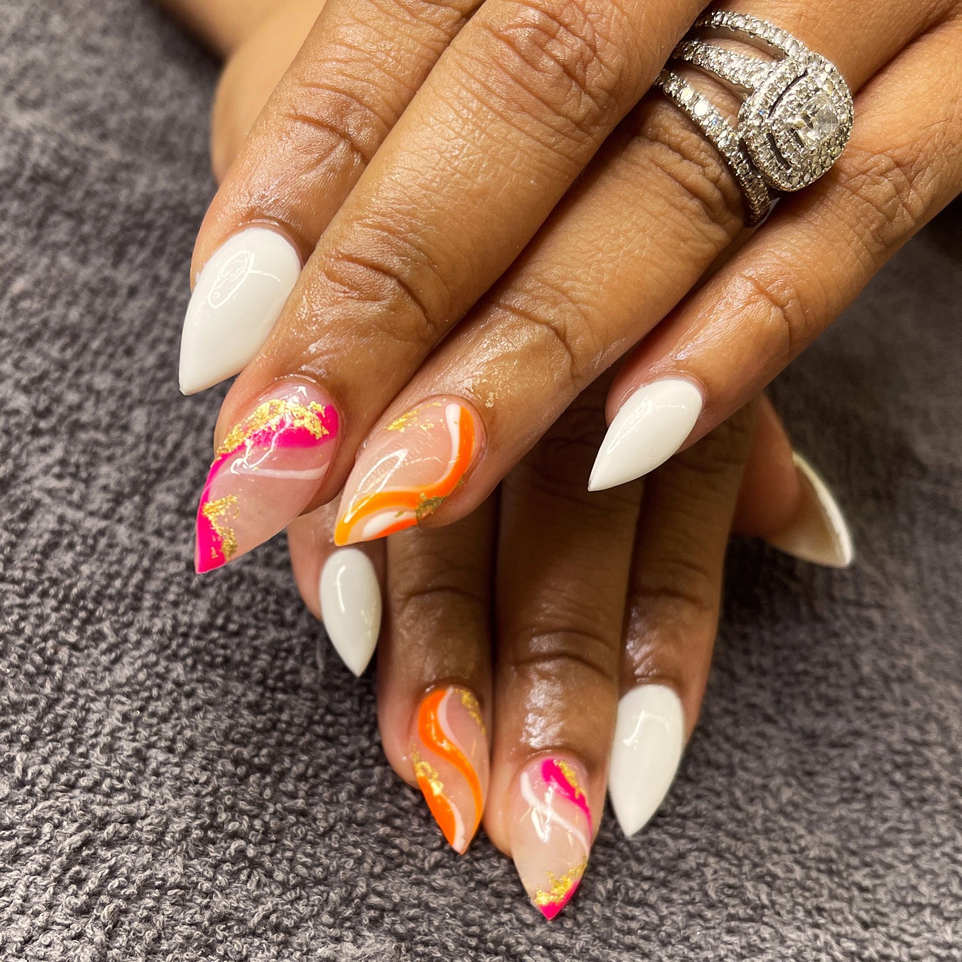 Manicured hands with white, pink, and orange nail art and a diamond ring on a gray textured surface