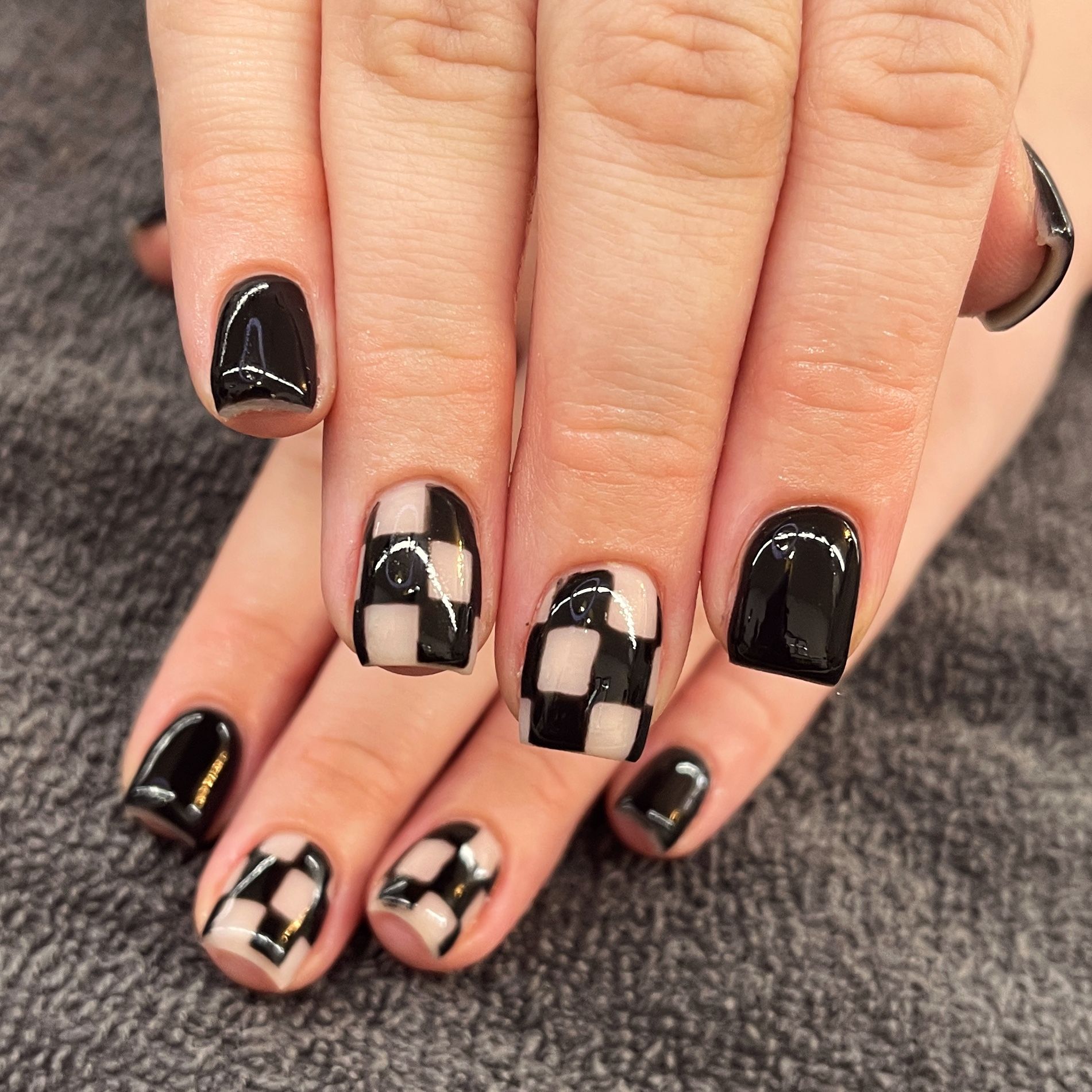 Close-up of hands with black and white checkerboard nail art on a gray fabric background