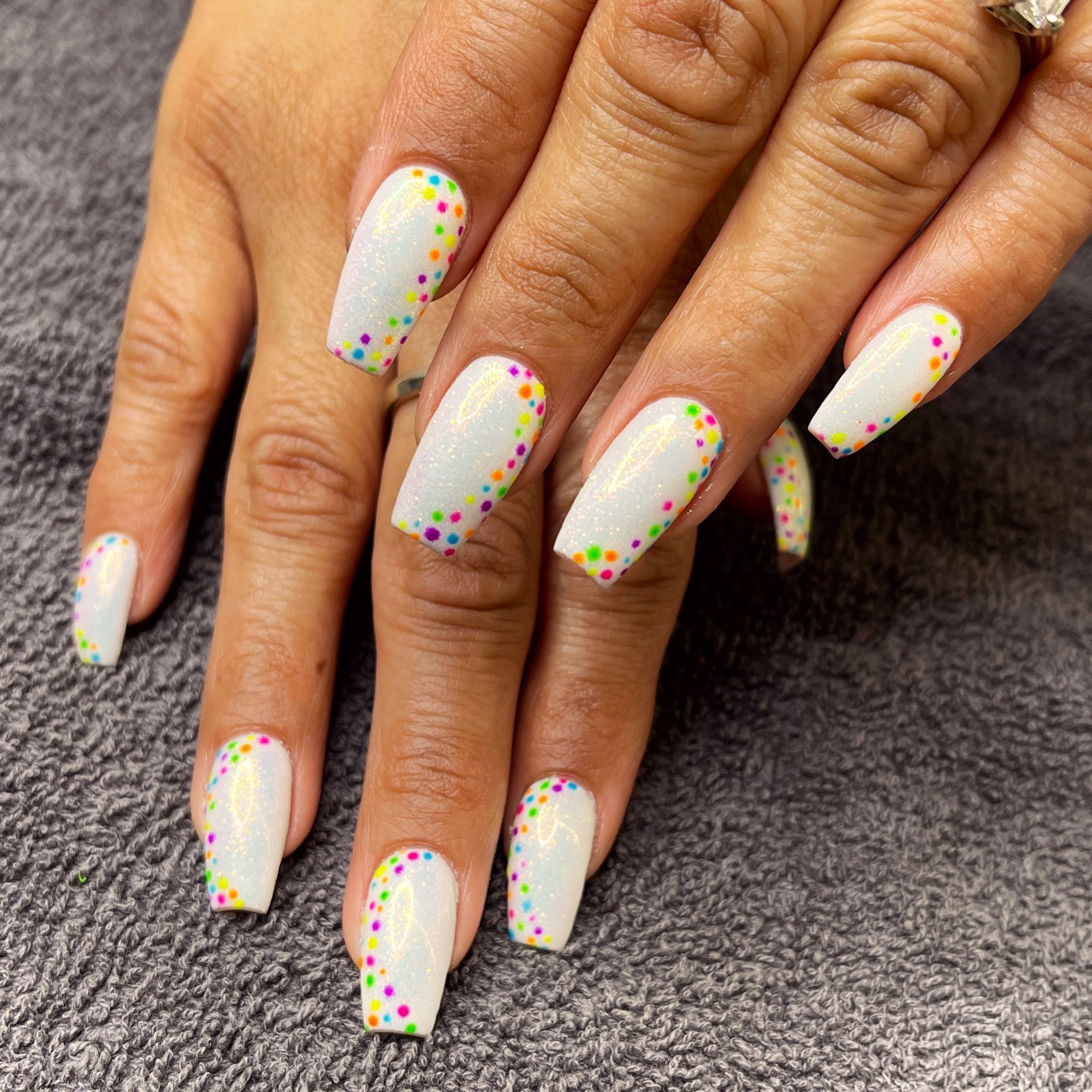 Hands with white nails and colorful dotted French tips on a gray surface