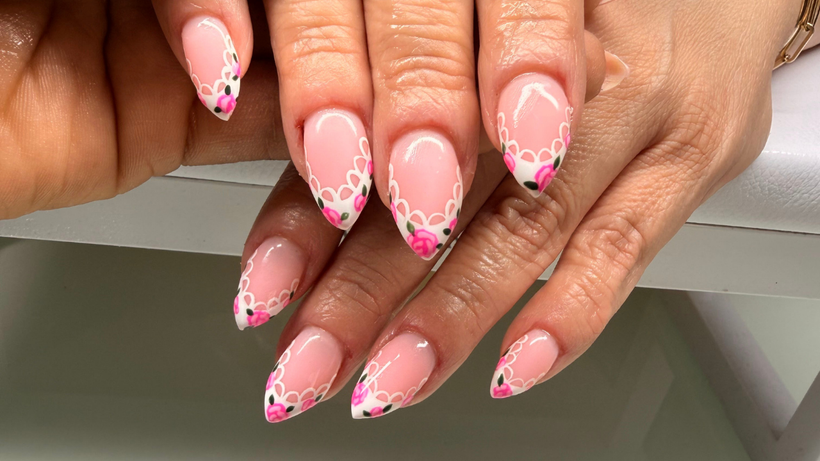 Hands with pink-and-white floral French-tip nails resting on a white surface