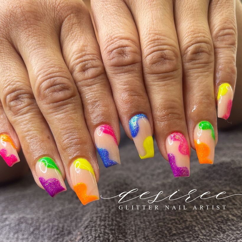 Hands with multicolored glitter gradient manicure and long square nails on a gray surface