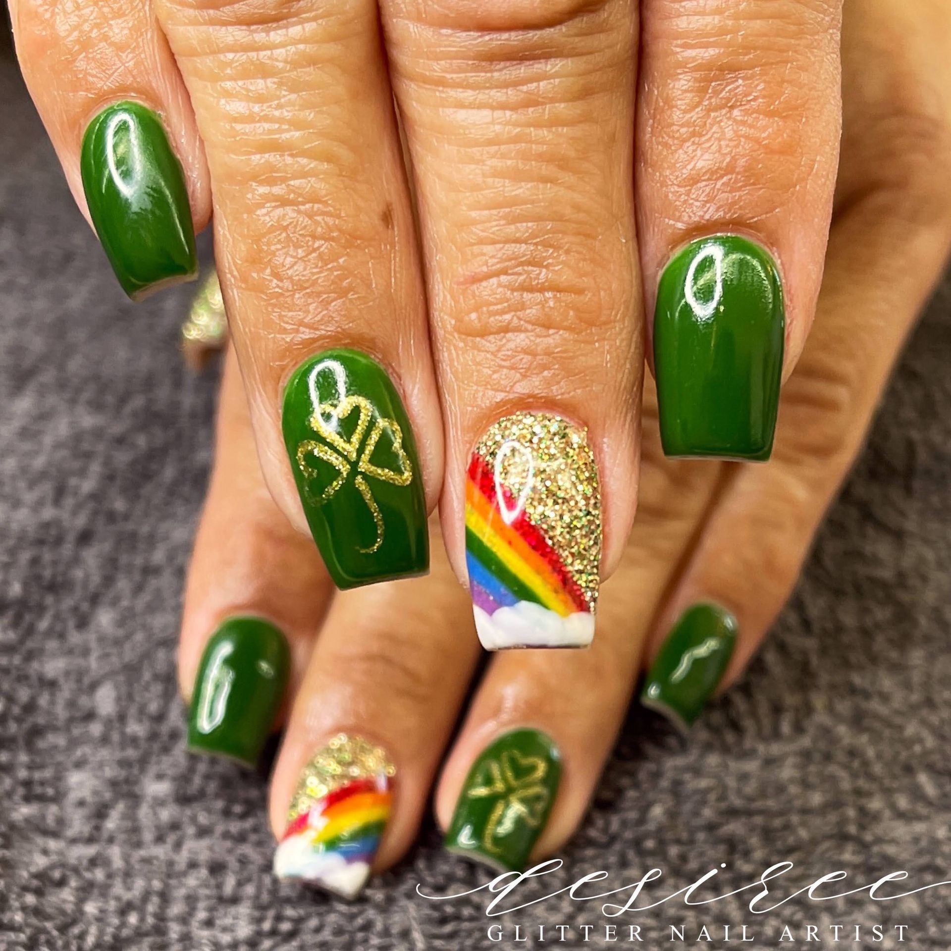Hands with green and gold manicure, featuring rainbow accent nails and gold ribbon nail art.