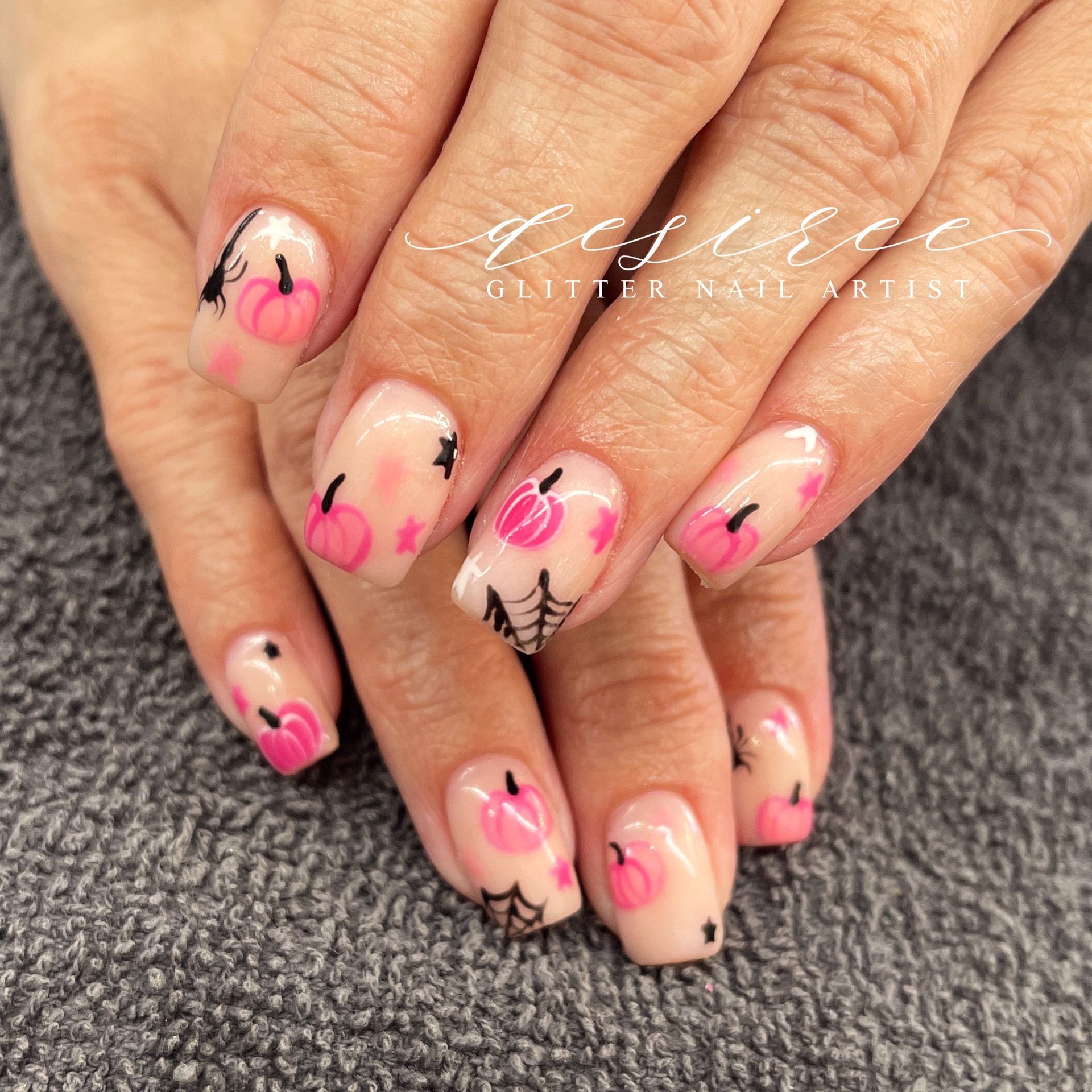 Hands with pink and black nail art resting on a gray textured surface