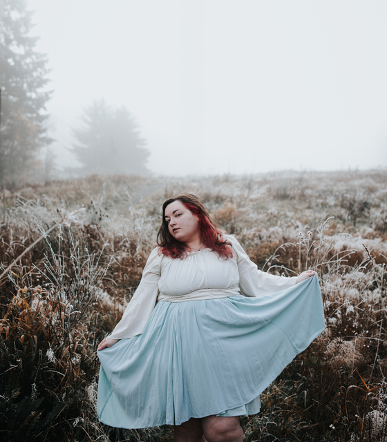 Woman in light blue dress holds up skirt in misty field.
