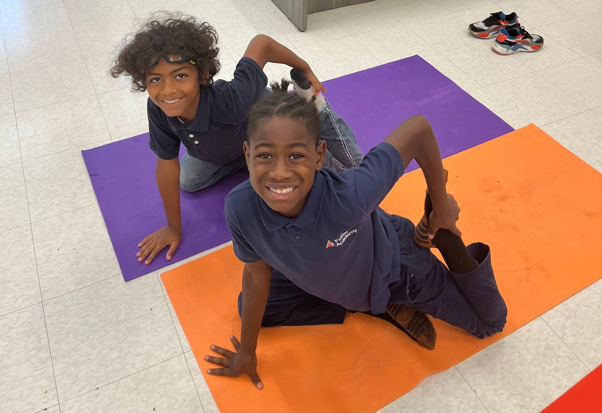Two young boys are sitting on yoga mats on the floor.