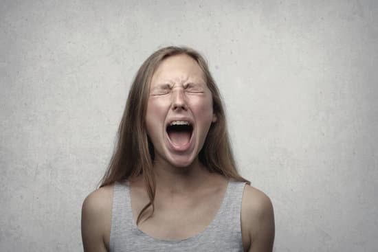 Woman with eyes closed and mouth wide open, appearing to scream against a plain gray background